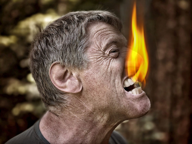 Mann mit brennendem Stück Kohle zwischen den Zähnen